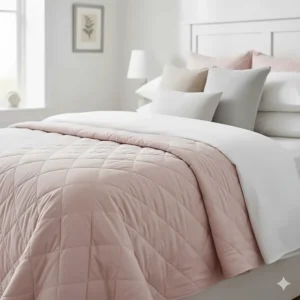 A blush pink quilted throw blanket layered over white bedding for a cosy bedroom look.