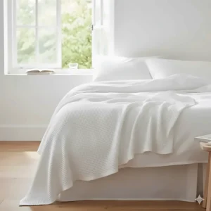 A lightweight white cotton blanket layered on a bed, perfect for cool summer nights in the UK.