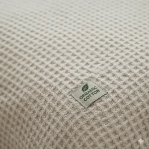 Close-up detail of the tight herringbone weave of a 100% organic cotton blanket.