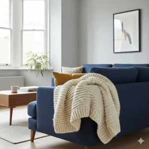 A cream 100% pure wool blanket draped over the arm of a navy blue fabric sofa in a modern British living room.