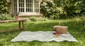 A breathable sage green organic cotton blanket used as a picnic rug in a blooming British garden.