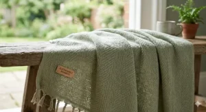 Close-up of a sage green sustainable bamboo eco-friendly blanket with a herringbone weave and a wooden Sustainable Bamboo label.