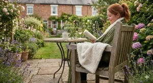 A woman wrapped in a dual sided blanket while reading in a lush British garden, ideal for staying warm during cool summer evenings on the patio.