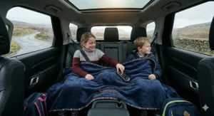 Two children in the back seat of a car sharing a large navy blue car heated blanket on a school run.