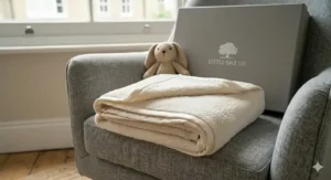 A plush, cream-coloured fleece blanket from the newborn gift set, draped over the arm of a nursery chair.