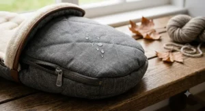 Close-up of the water-resistant outer fabric on a grey quilted pram footmuff, featuring precise stitching and realistic water droplets beading on the surface.