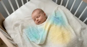 A baby sleeping soundly under a light, breathable baby blanket in a nursery.
