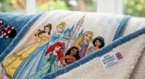 A soft, plush Disney throw blanket draped over a grey sofa in a brightly lit living room.