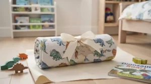 A rolled-up dinosaur blanket for boys tied with a festive gift ribbon, ready for giving as a birthday present.