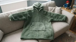A neutral-fitting dinosaur hoodie blanket laid flat to showcase its roomy, oversized design suitable for boys and girls.