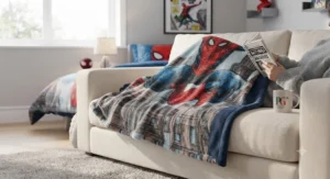 A person snuggling under a cosy Spider-Man fleece blanket on the sofa while reading a book.