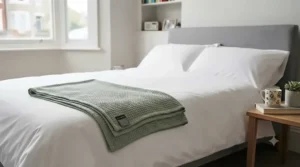 A neatly made double bed styled with a crisp white duvet and a folded lightweight blanket under £20 at the foot of the bed.