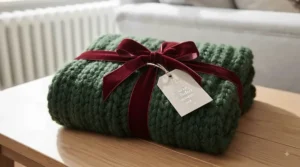 A neatly rolled chunky knit Christmas throw tied with a festive velvet ribbon, ready to be given as a winter homeware gift.