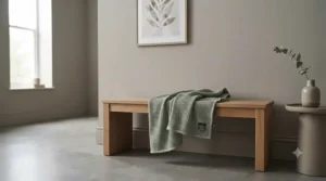 A minimalist bedroom interior featuring a neutral-toned lightweight blanket under £20 hung gracefully over a wooden bench.