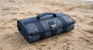 Compact foldable picnic blanket rolled up with a convenient carry handle for easy transport to the seaside.