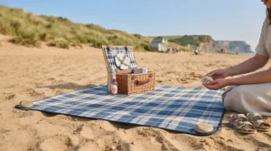 A sand-free family picnic blanket laid out on a sandy British beach with dunes in the background.