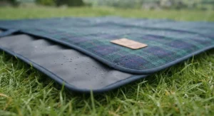 Close-up of the waterproof backing on a travel picnic rug resting on damp grass, keeping users dry.
